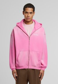 Lys rosa zip-up hettegenser med gradienteffekt, med kengurulomme, ribbede mansjetter og en logo trykt på brystet.