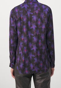 Langärmliges Hemd aus schwarzem Stoff mit lila floralem Muster und roten Akzenten. Verfügt über einen Button-Down-Kragen und Ein-Knopf-Manschetten.