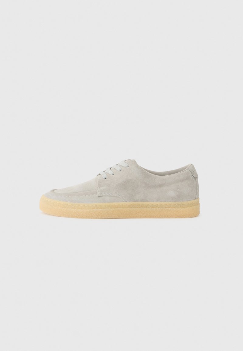 Gray suede sneaker with a round toe, lace-up design, and a textured rubber sole in a contrasting beige color. Minimalistic style.