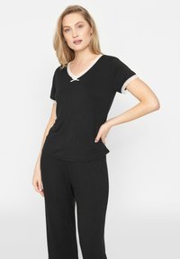 Ensemble de détente noir comprenant un haut à manches courtes avec dentelle et décolleté en V, associé à un pantalon ample. Texture de tissu douce.