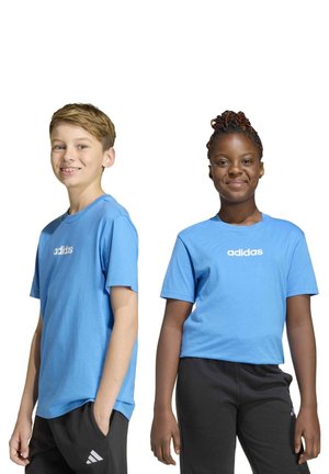 Deux enfants souriants portent des T-shirts Adidas bleus assortis et des pantalons noirs sur fond blanc.