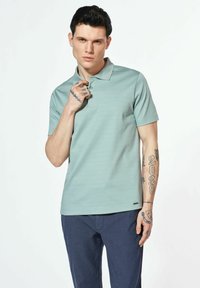 Koszulka polo w jasnym odcieniu teal z delikatnymi poziomymi paskami, z trzygurowym zapięciem i krótkimi rękawami, w połączeniu z granatowymi spodniami.