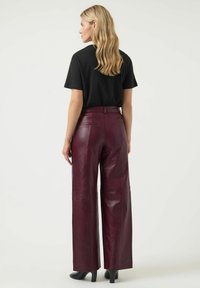 Bordeaux leren wijde broek met een gladde textuur, voorzien van achterzakken en een hoge taille, gecombineerd met een eenvoudige zwarte t-shirt.