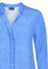 Blå långärmad skjorta med krage, prydd med ett prickigt mönster i vitt. Tillverkad av lättviktigt tyg; inkluderar knappstängning fram.