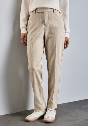 Beige mönstrade byxor med skräddarsydd passform, med framfickor och knäppning, i kombination med vita och beige sneakers.