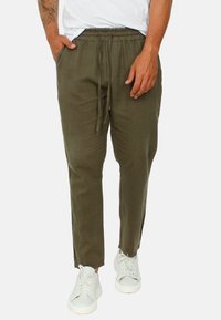 Pantaloni in lino leggero di colore verde oliva con vita elasticizzata, tasche laterali e una vestibilità affusolata, abbinati a sneakers bianche.