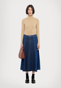 Šviesiai smėlinis turtleneckas, mėlynos džinsinės maxi sijonas su priekinėmis siūlėmis ir juodi loaferiai. Laikoma ruda rankinė. Lygi tekstūra, kasdieniškas dizainas.
