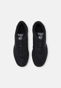 Černé semišové tenisky s kulatou špičkou, šněrováním vpředu a perforovanými detaily. Obsahují logo Reebok na jazyku a bočním panelu.