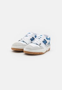 Chaussures de sport blanches avec un bout en daim, des accents bleus, un col matelassé et une semelle en caoutchouc naturel. Le numéro de modèle 550 est affiché sur le côté.