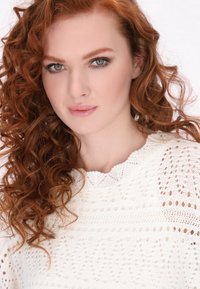 Maglione bianco lavorato a maglia con scollatura a ondina, caratterizzato da motivi intricati e una finitura testurizzata, indossato da una persona con capelli rossi ricci.