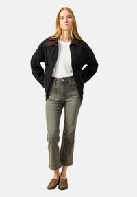 Czarna kurtka z brązowym kołnierzem z kordurowego materiału, biała koszulka, szare spodnie z wysokim stanem i buty wsuwane w leopardzi wzór.