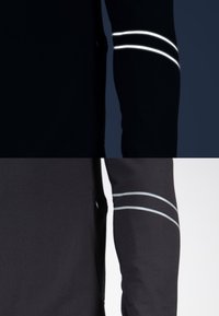 Zwart sportief longsleeve shirt met reflecterende witte accenten op de bovenarm, met een soepele textuur en een aansluitend ontwerp.