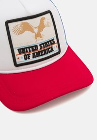 Gorra roja y blanca con un diseño estructurado. Presenta un parche rectangular con un gráfico de un águila dorada y el texto: "OREGON STATE ESTADOS UNIDOS DE AMÉRICA."