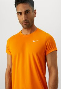 Orange atletisk t-shirt med korte ærmer, lavet af et glat, let materiale. Har et lille hvidt Nike-logo på brystet.