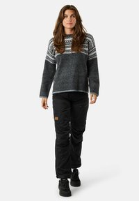 Maglione di lana lavorato a maglia di colore grigio scuro con motivo nordico in grigio chiaro e bianco, abbinato a pantaloni cargo neri e sneakers nere.