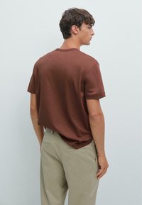 Bruine T-shirt met korte mouwen gemaakt van zacht katoen, met een comfortabele pasvorm en een ronde hals, gecombineerd met lichtbeige broek.