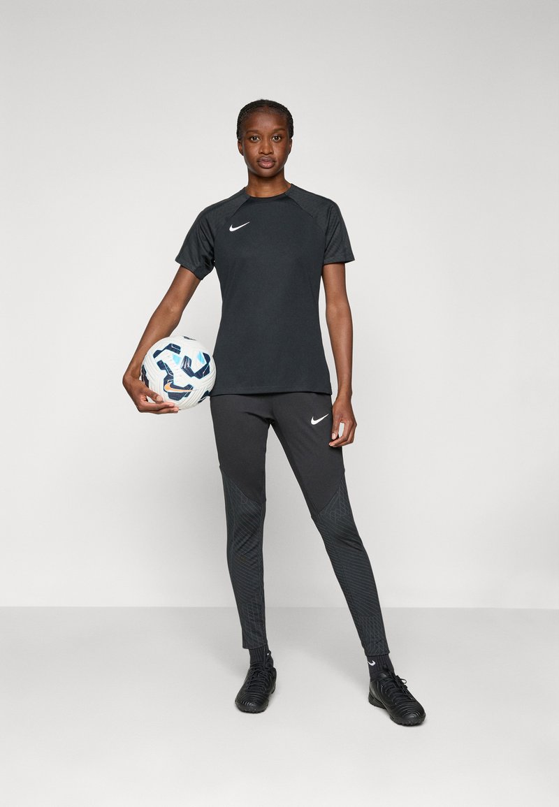 Maglietta sportiva nera Nike con maniche corte e leggings neri abbinati con dettagli testurizzati, mentre tiene un pallone da calcio con un motivo.