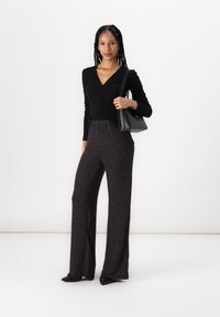 Black long-sleeve top with a v-neck, paired with wide-leg, textured pants in dark tones featuring subtle multicolor flecks. Black handbag.