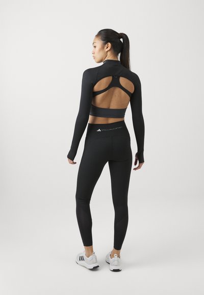 Un conjunto atlético negro que incluye una camiseta recortada de manga larga con cortes y leggings de talle alto, combinado con zapatillas deportivas blancas.