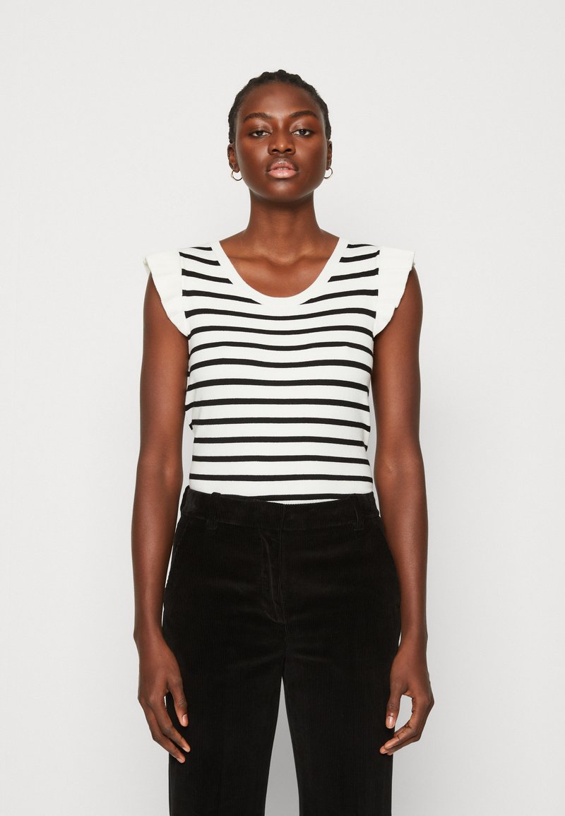 Schwarzes und weißes gestreiftes ärmelloses Oberteil mit rüschenbesetzten Schulterakzenten, kombiniert mit schwarzen Corduroyhosen. Glatte Stoffoberfläche.