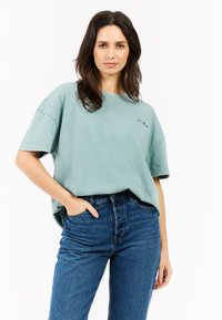 Lichtgroen oversized t-shirt met korte mouwen en een ronde hals, gecombineerd met hoge blauwe denim jeans, met een zichtbaar voorvak.