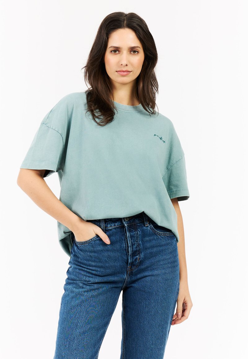 Lichtgroen oversized t-shirt met korte mouwen en een ronde hals, gecombineerd met hoge blauwe denim jeans, met een zichtbaar voorvak.