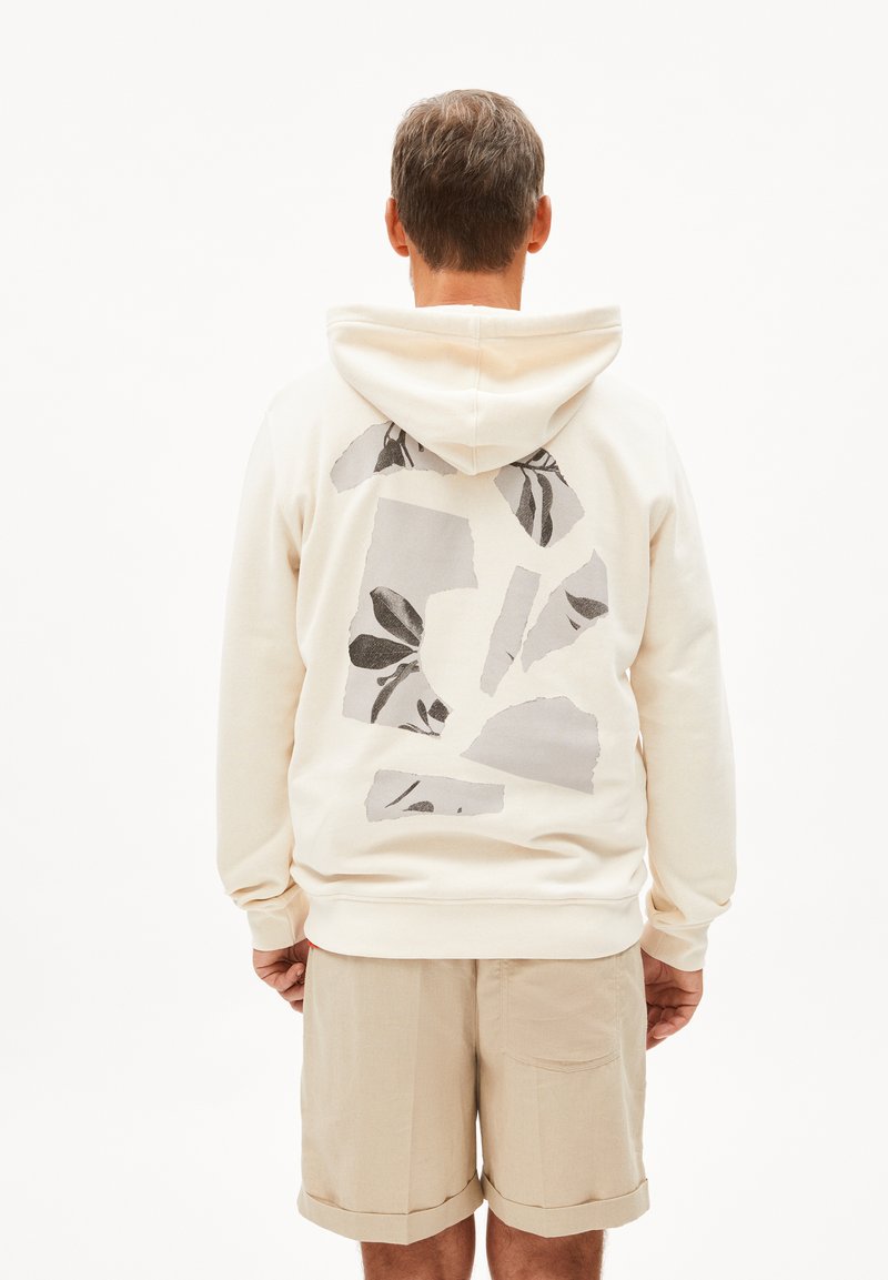 Felpa crema con una grande stampa floreale astratta in grigio e nero sulla schiena; abbinata a pantaloni corti beige chiaro e polsini elastici.