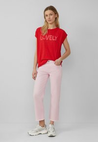 T-shirt rouge à manches courtes avec l'imprimé "LOVELY", associé à un jean droit rose clair et des baskets gris-blanc. Tenue simple et décontractée.