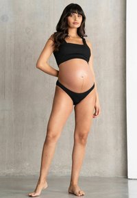 Conjunto de bikini premamá negro con canalé que incluye un top corto de cuello cuadrado con tirantes gruesos y braguitas tipo tanga de talle bajo. Tejido suave y elástico.
