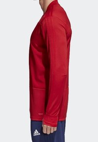 Maillot de sport rouge à manches longues avec un col rond, fabriqué en matériau léger. Comprend des détails de coutures et des poignets ajustés.