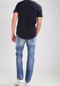 Tumma laivastonsininen lyhythihainen t-paita, vaaleansiniset kulutetut farkut, valkoiset tennarit mustilla yksityiskohdilla, nähtynä takaa.