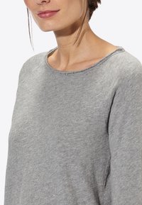 Pullover grigio a maniche lunghe con scollatura rotonda, realizzato in un morbido tessuto testurizzato e con dettagli a taglio vivo al colletto e alle spalle.