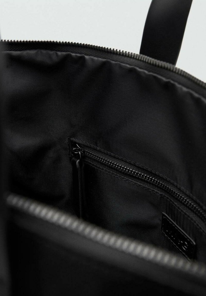 Interno dello zaino nero con tessuto in nylon, tasca con zip e texture liscia. Dettagli con zip lungo il bordo superiore.