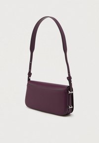 Bolsa de ombro roxa em pele, com alça ajustável e detalhes de fivela prateada, apresentada contra um fundo claro e liso.