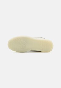 Hvit gummisåle til sneakers med teksturert mønster, som har en avrundet form og logo-detall. Glatt overflate med en lysfarget base.