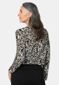 Langarm blouse in een licht beige en zwart abstract patroon, gemaakt van lichte stof met een gladde textuur en een eenvoudig ontwerp.
