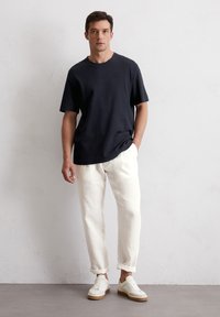 Czarny granatowy T-shirt w połączeniu z białymi lnianymi spodniami. Sneakersy mają białą cholewkę i brązową podeszwę. Prosty, luźny krój z podwiniętymi mankietami.