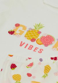 Bílý bavlněný outfit s grafikou "Good Vibes" a ovocnými a květinovými potisky. Obsahuje krátký rukáv a vzorované šortky.