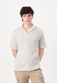Camisa de manga corta con botones en una tela ligera y texturizada, con un sutil patrón en ondas en tonos crema y azul claro. Con cuello.