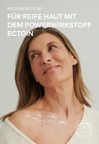 Anti-aging skincare product with text on skin, featuring a light cream sweater, natural hair, and neutral background.
