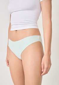 Bañador de bikini de color verde claro, sin costuras, con una textura suave y un diseño de tiro bajo, que presenta un corte minimalista y una tela suave.