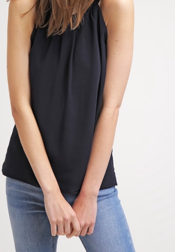 Blusa sin mangas de color negro con escote fruncido, hecha de una tela ligera. Combinada con jeans de color azul claro, que muestran un ajuste relajado.