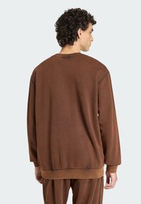 Hnedý, nadrozmerný sveter s okrúhlym výstrihom, rebrovanými manžetami a lemom. Mäkka textúra, uvoľnený strih a viditeľné švy.