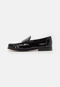 Mustad musta lakitud nahast loafers, millel on kortsus eesmine osa, lame konts ja dekoratiivne metalldetail peal. Sile tekstuur, klassikaline disain.