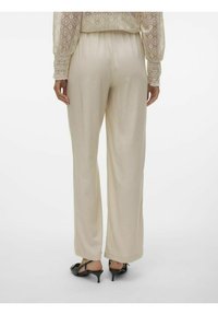 Pantalons larges beige en tissu lisse et doux. Taille élastique et ourlet à la cheville. Portés avec des chaussures à talons noires.