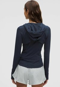 Jūras spēku tumši zils garās piedurknes kapuce ar kapuci un izšūtām akcentiem, apvienota ar gaiši pelēkiem šortiem. Mīksts, elastīgs audums, kas piemērots aktīvai lietošanai.