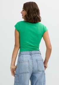 Top verde de manga corta combinado con pantalones cargo de mezclilla azul claro de talle alto, que cuentan con múltiples bolsillos y un corte relajado.
