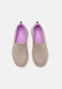 Sapatilhas desportivas slip-on em malha castanha clara com uma superfície texturizada. O interior conta com uma palmilha acolchoada roxa e sola de borracha flexível.
