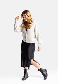 Biała dziergana kardigan z dużymi guzikami, noszony na czarną spódnicę slip z bocznym rozcięciem, w zestawieniu z czarnymi, sznurowanymi butami wojskowymi.