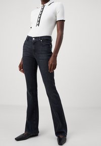Polo blanc à côtes avec bord noir, doté d'une patte de boutonnage ; associé à un jean évasé foncé et des chaussures à bout carré noires.